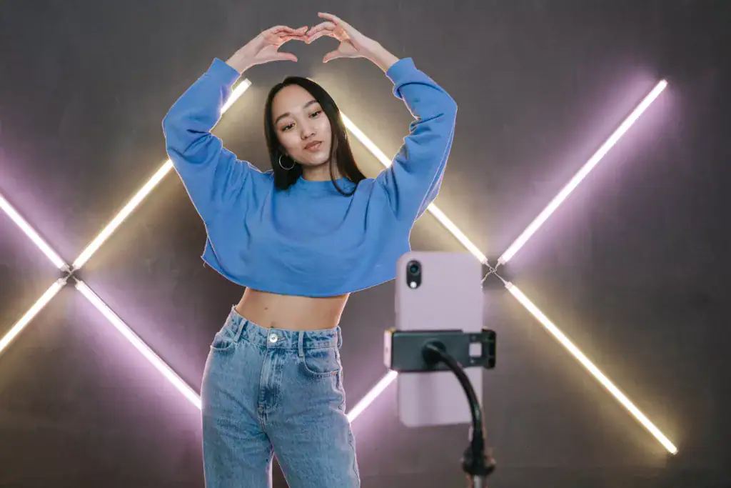 Young woman in blue sweatshirt taking a selfie with neon lights background.