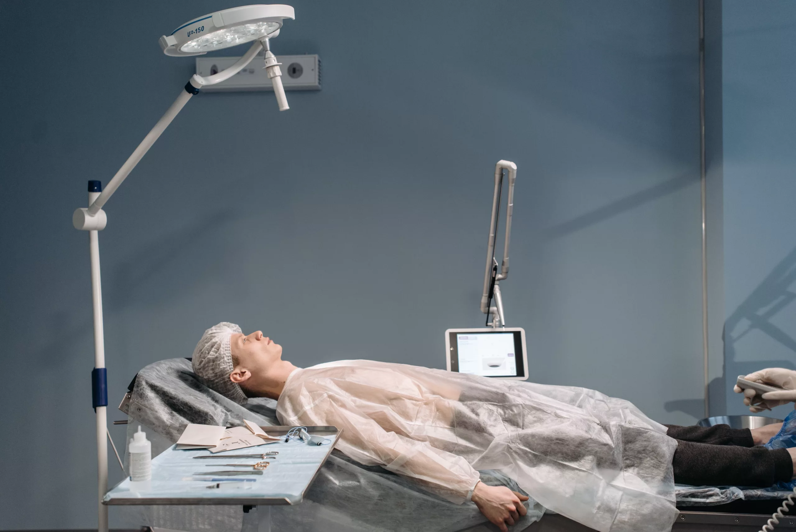Osoba leżąca na łóżku szpitalnym, otoczona sprzętem medycznym
